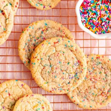 big and little cookies with round and stick sprinkles scattered on copper wire rack.