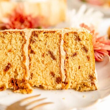 Close-up of Biscoff cake layers filled with Biscoff buttercream on white plate with flowers in background.