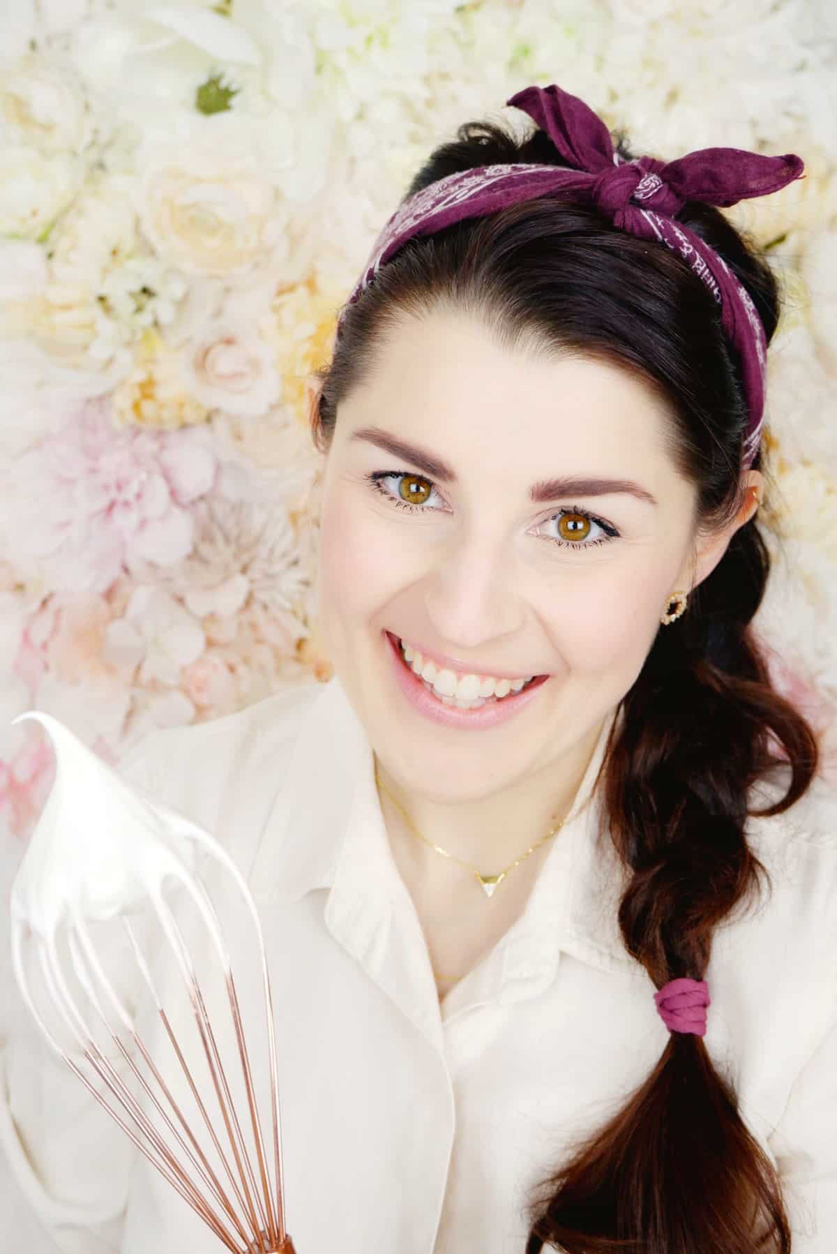 headshot of Jocelyn in front of flower wall with meringue-covered whist.