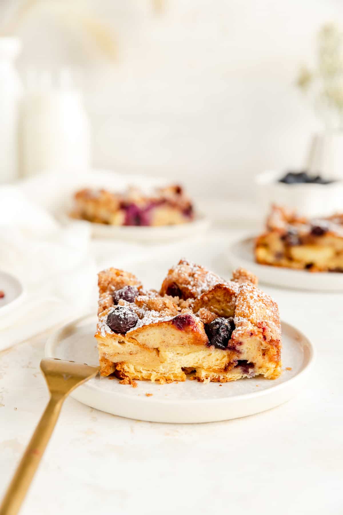 side view of french toast casserole with blueberries piece on plate with other pieces in background.