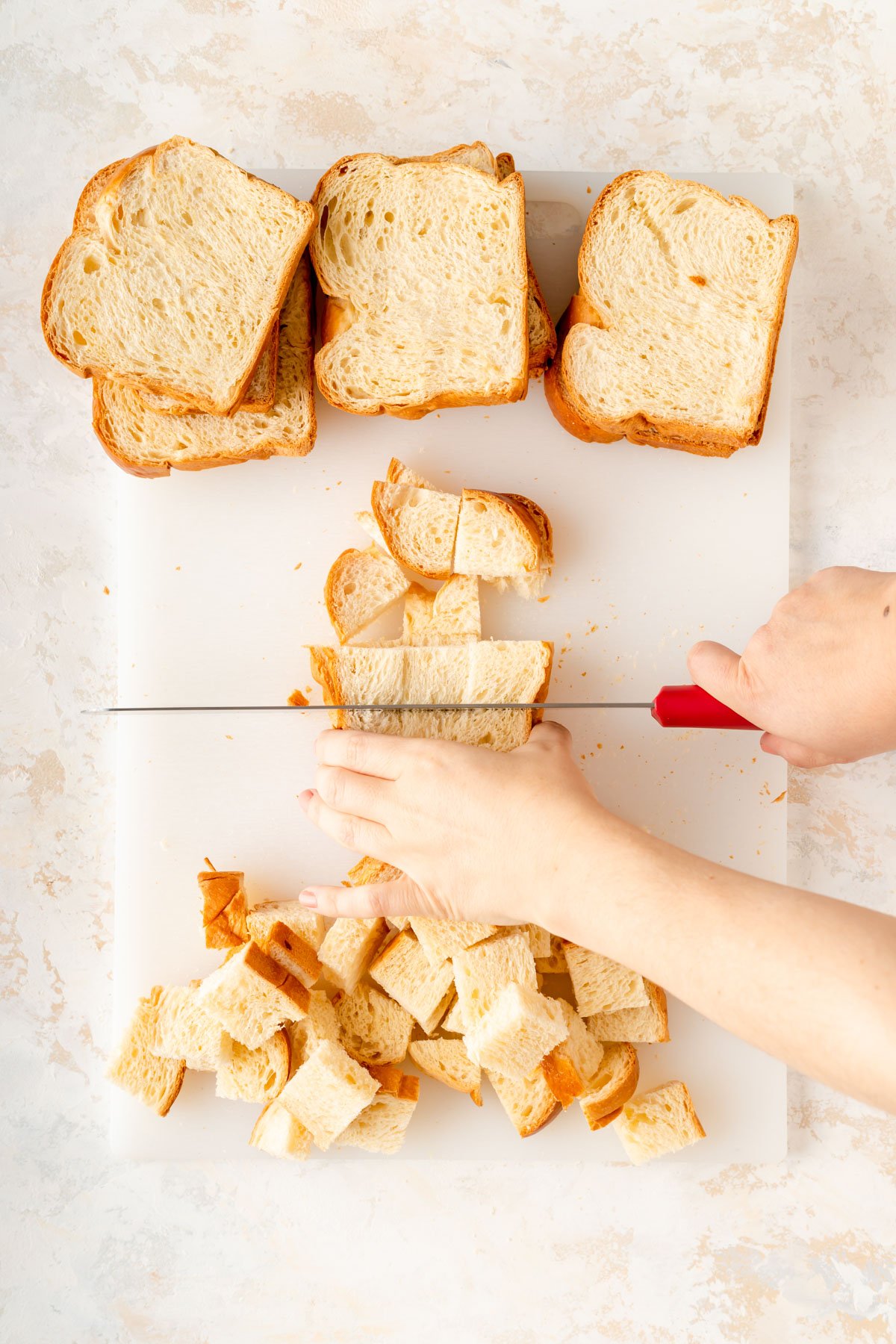 someone reaching into frame to cut brioche slices into cubes on a white cutting board.