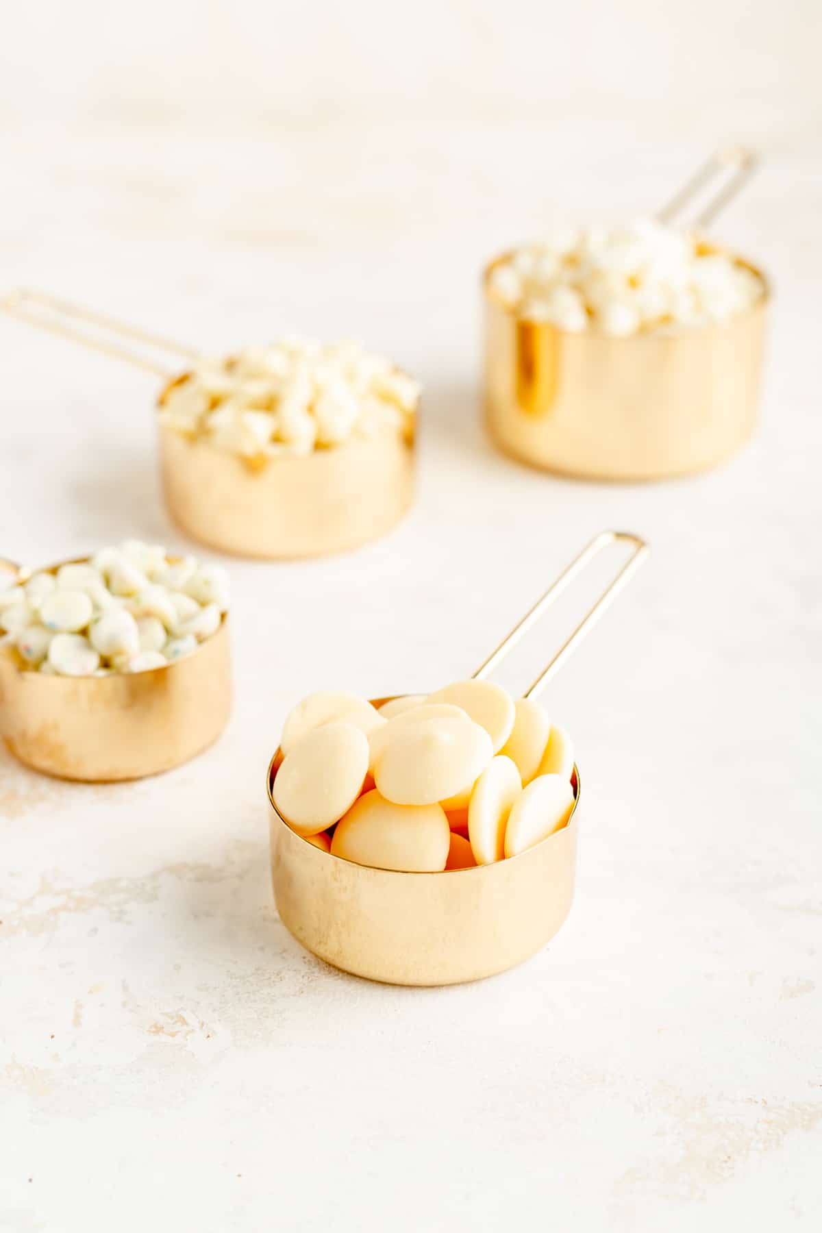 gold measuring cups filled with different white chocolate chips and pistoles.