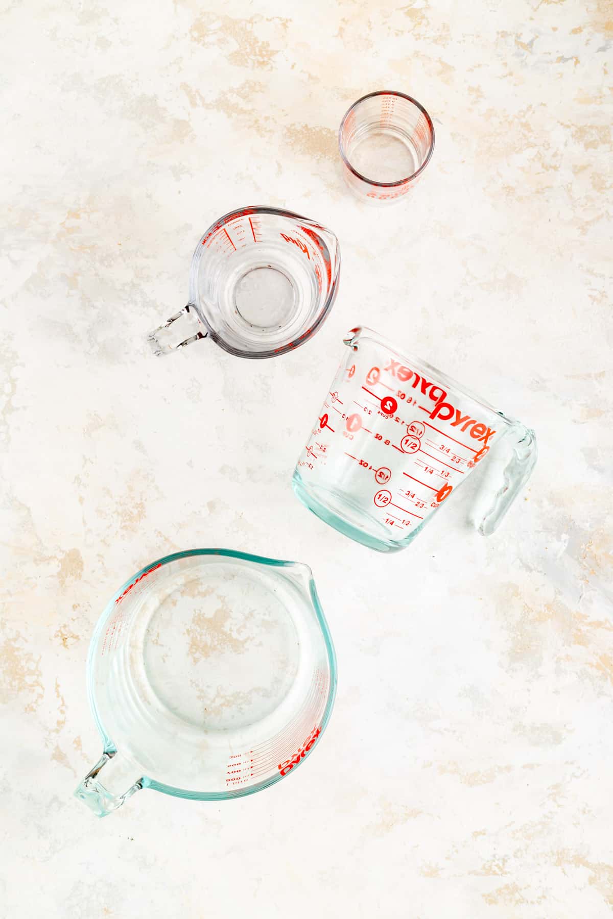 empty glass pyrex pitchers from above with one on its side on white plastic background.