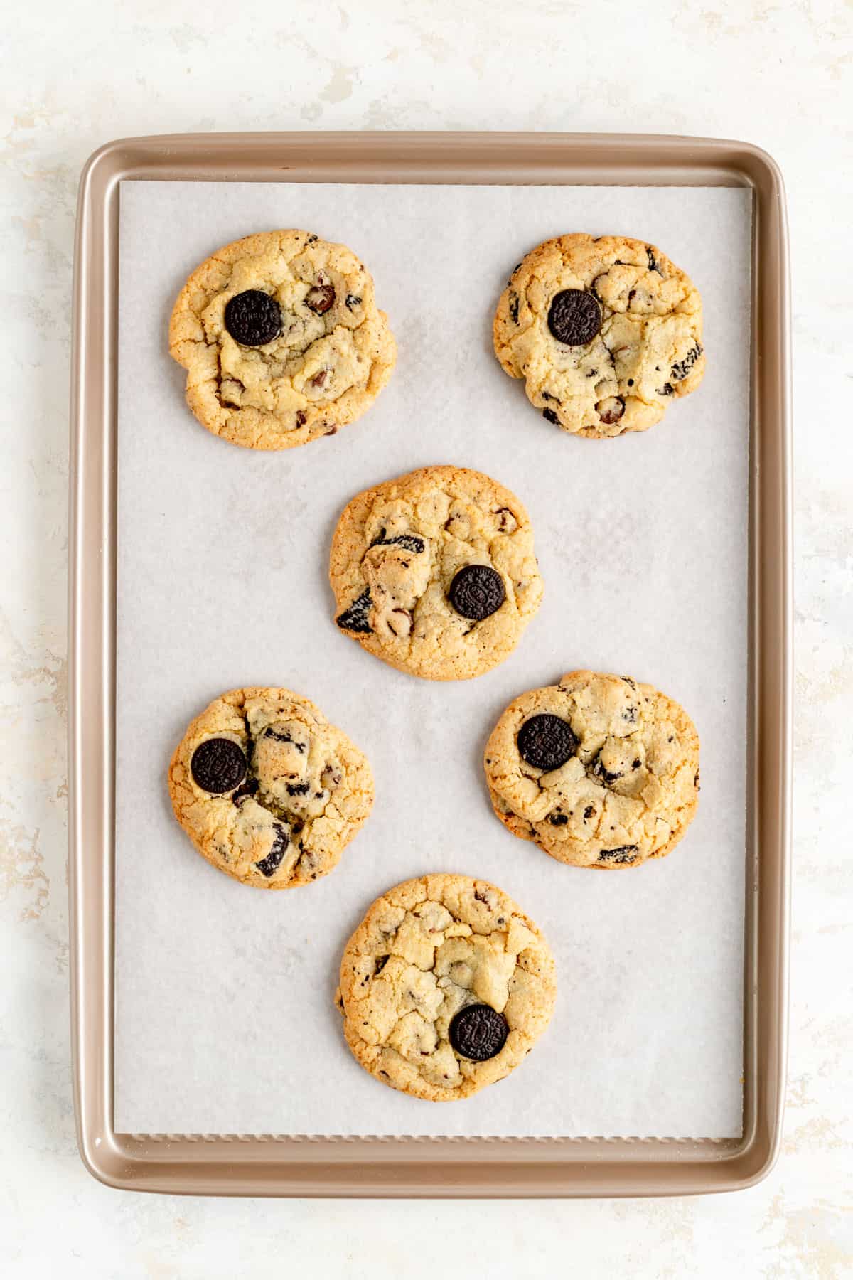 six baked oreo chocolate chip cookies on a parchment lined tan baking sheet.