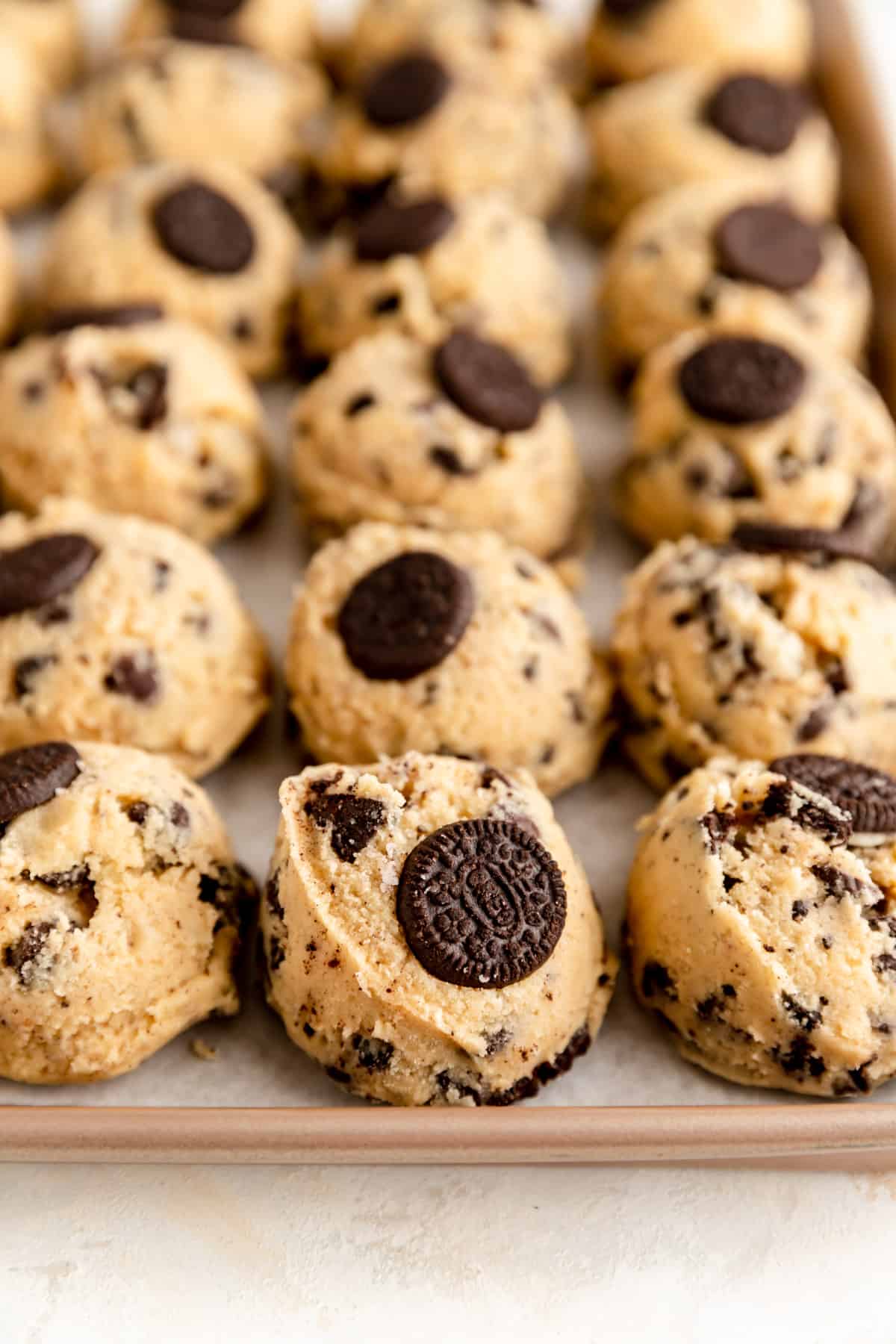 oreo chocolate chip cookie dough balls lined up on a tan baking sheet.