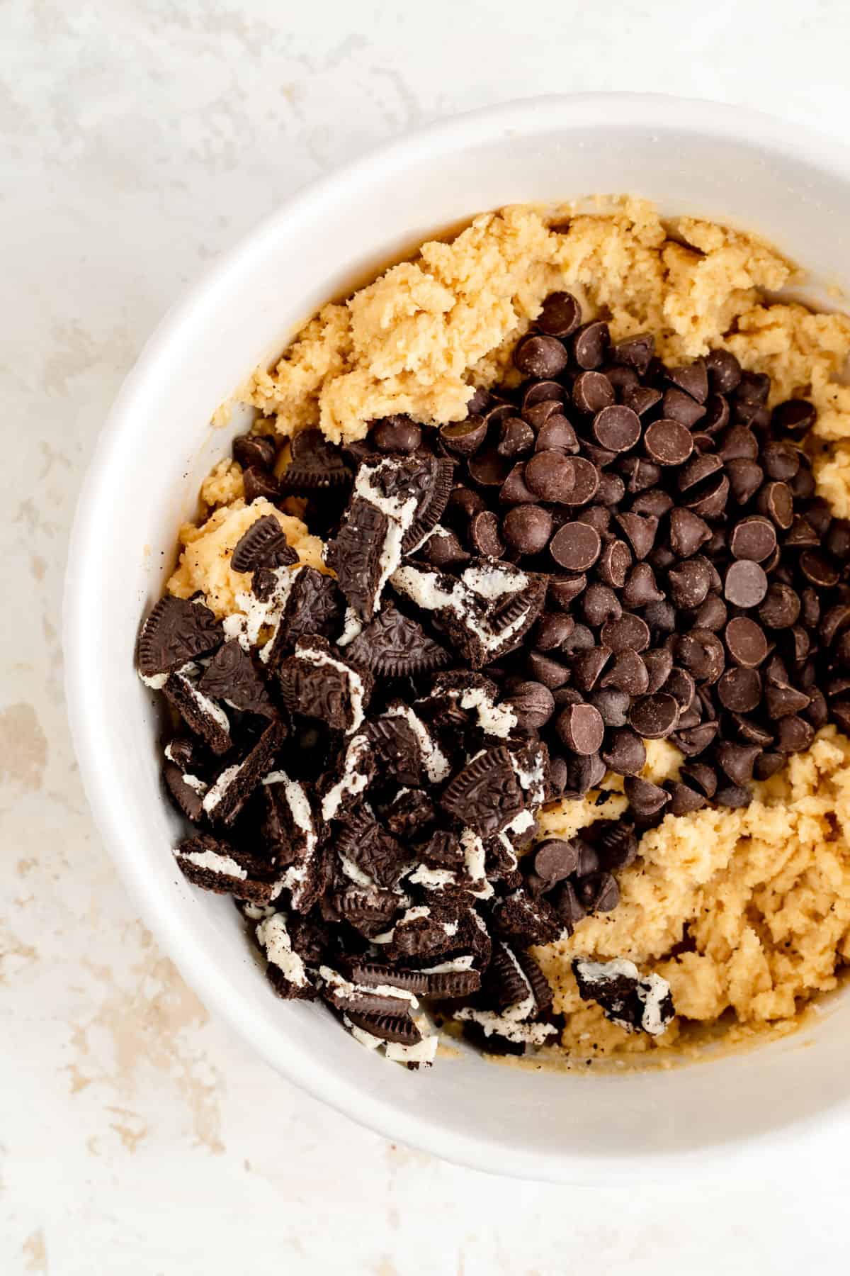 cookie dough in a white bowl with chocolate chips and crushed cookies on top.