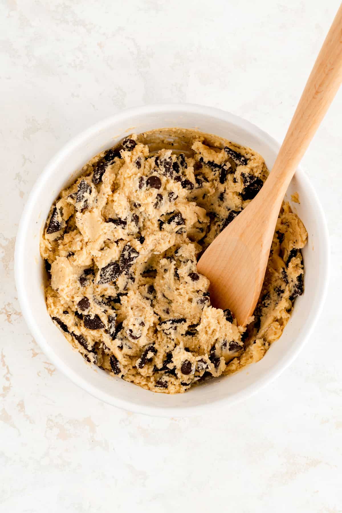 fully mixed oreos chocolate chip cookie dough in a white bowl with a wooden spoon in it.