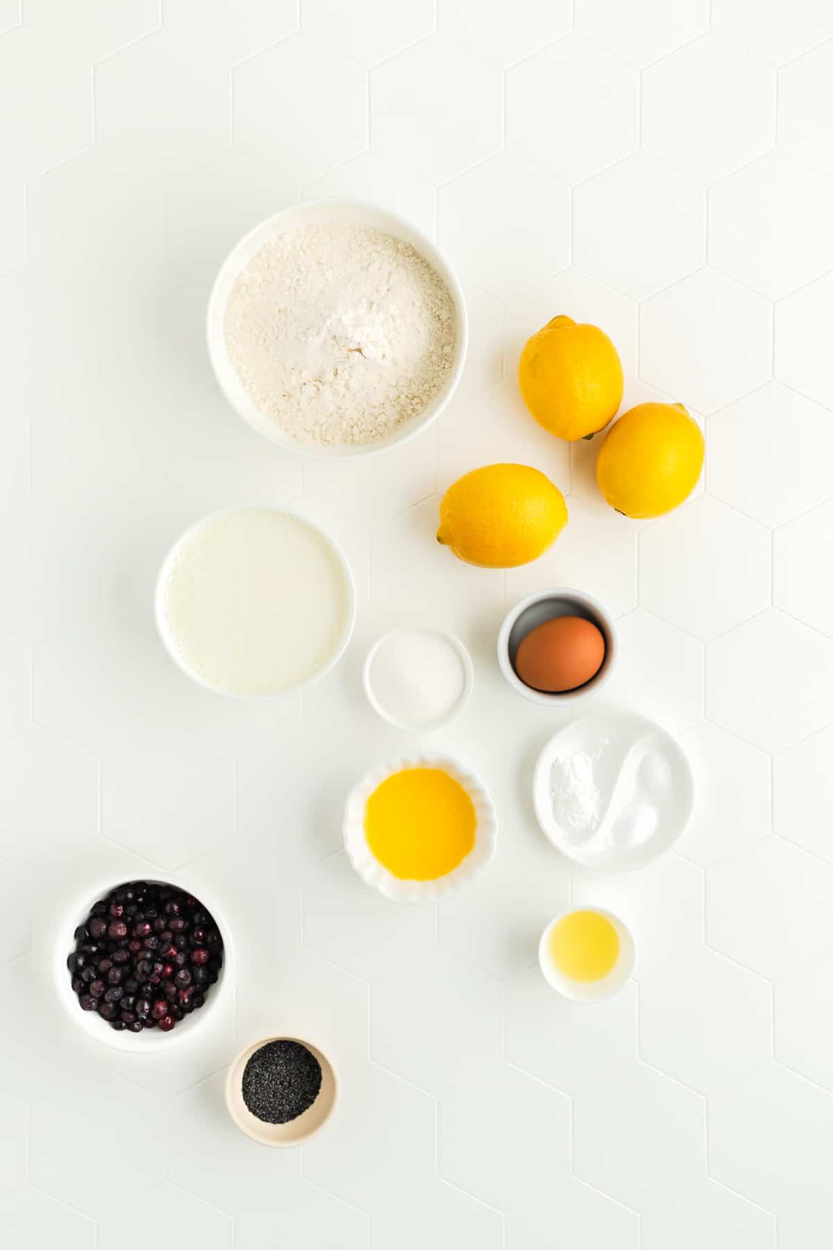 Ingredients for lemon pancakes in individual bowls on white background.
