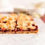 close up of raspberry oatmeal bar layers from the side on parchment paper.