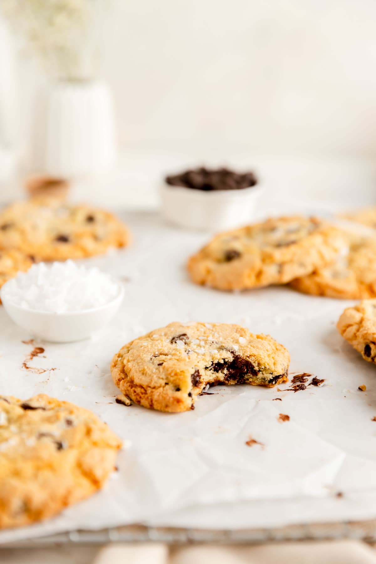 thick chocolate chip cookie with bite out and other cookies and ingredient bowls in background