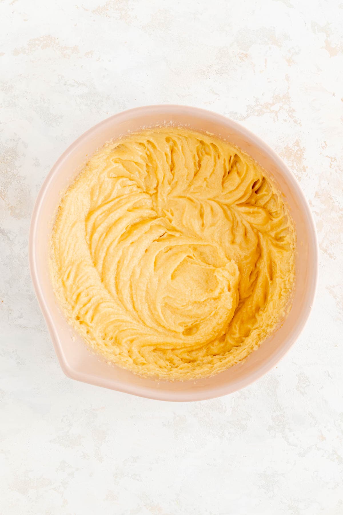butter sugar and egg batter mixed in tan bowl on white background