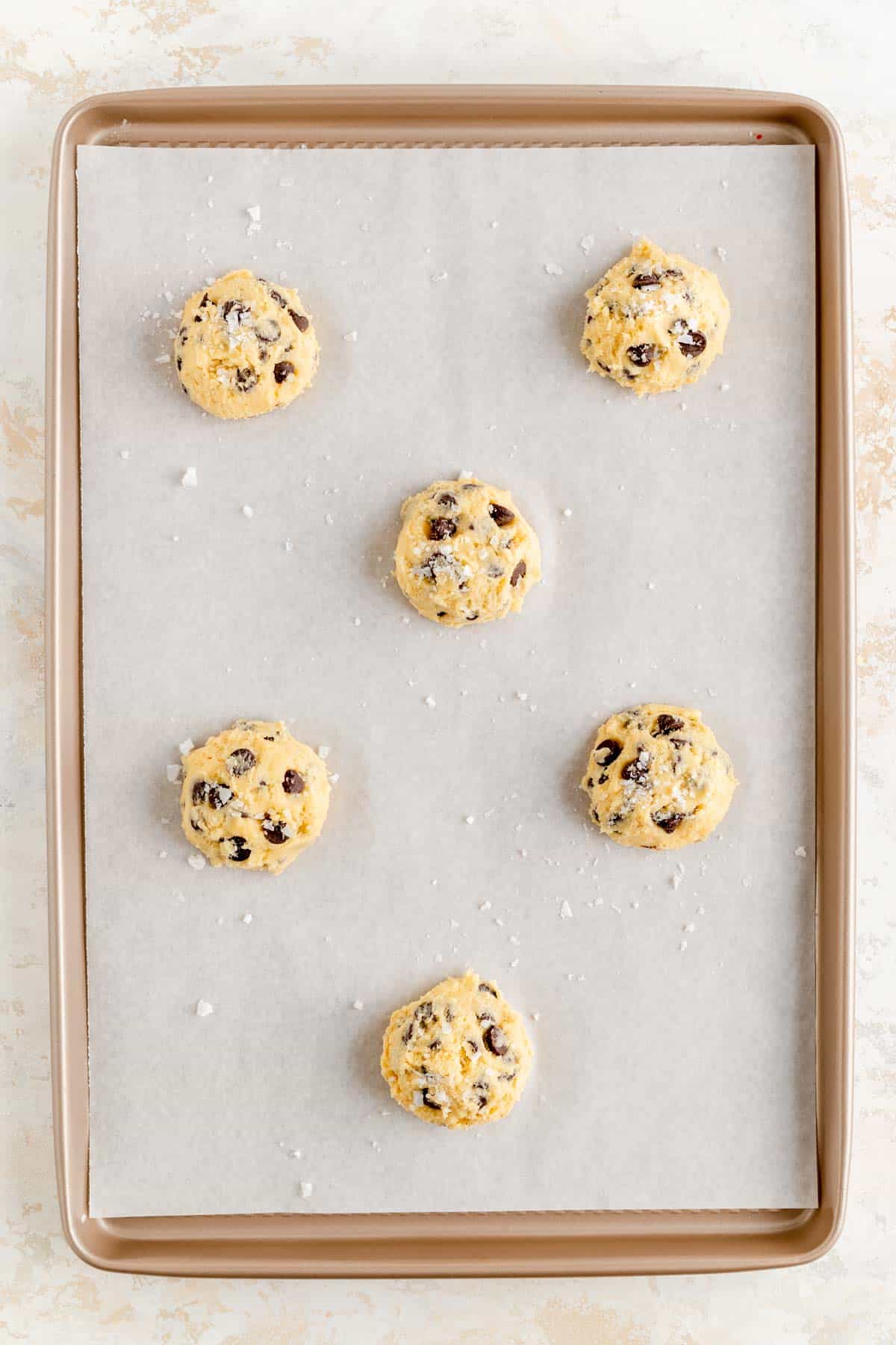 salted scooped chocolate chip cookie dough balls on parchment lined gold baking sheet