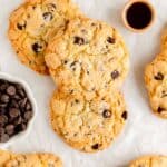 three chocolate chip cookies stacked on parchment paper surrounded by ingredients in bowls