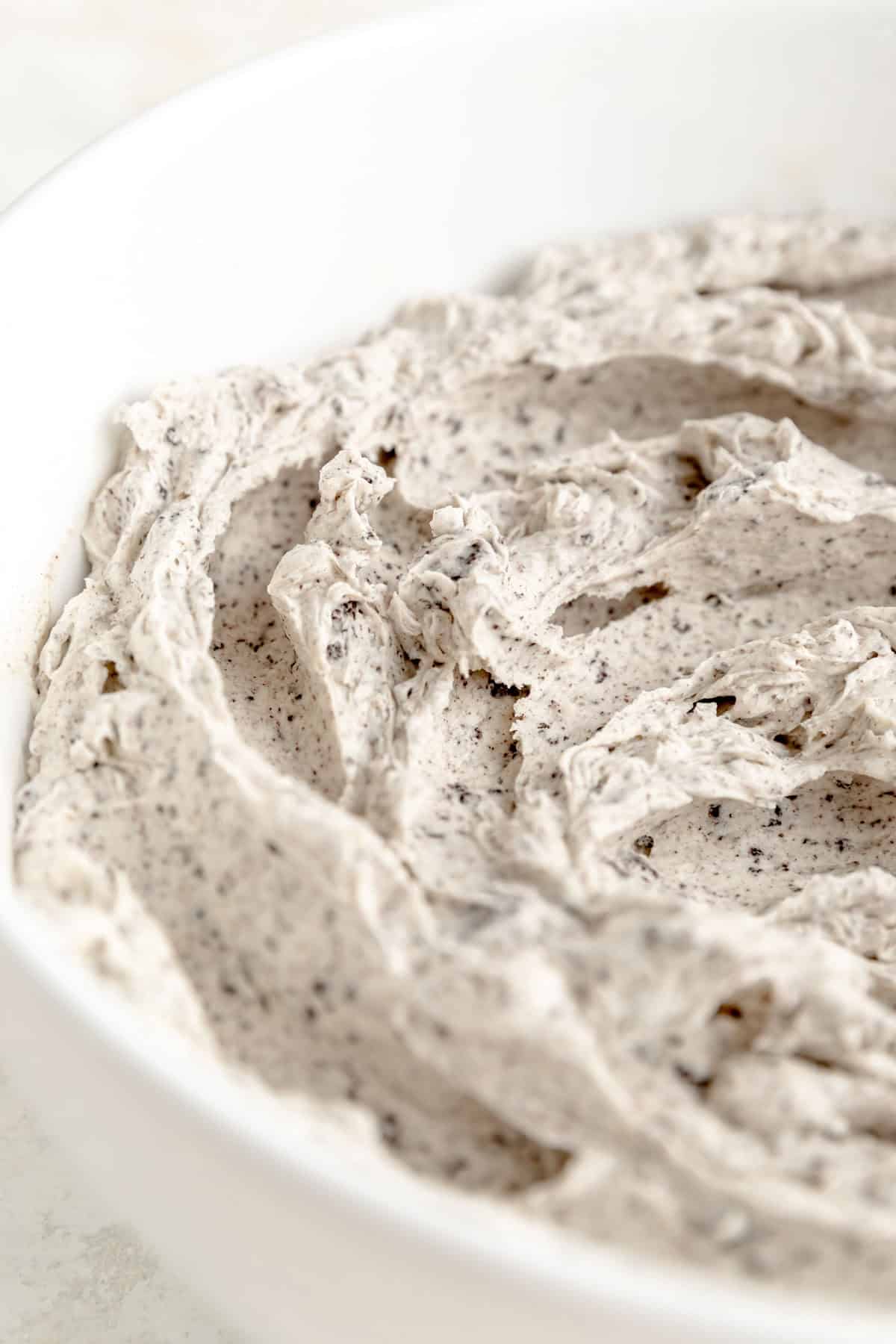 close up from side of swirled cookies and cream frosting in a white bowl.