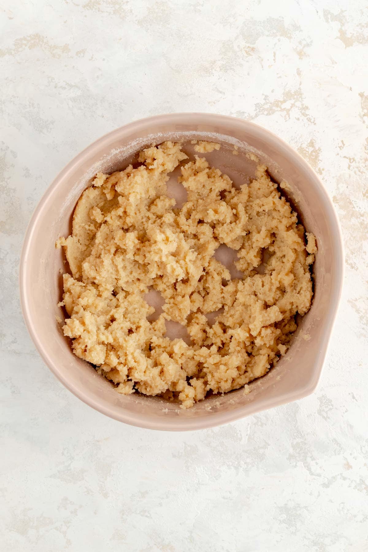 butter and sugar mixed in a tan bowl on white plaster background.