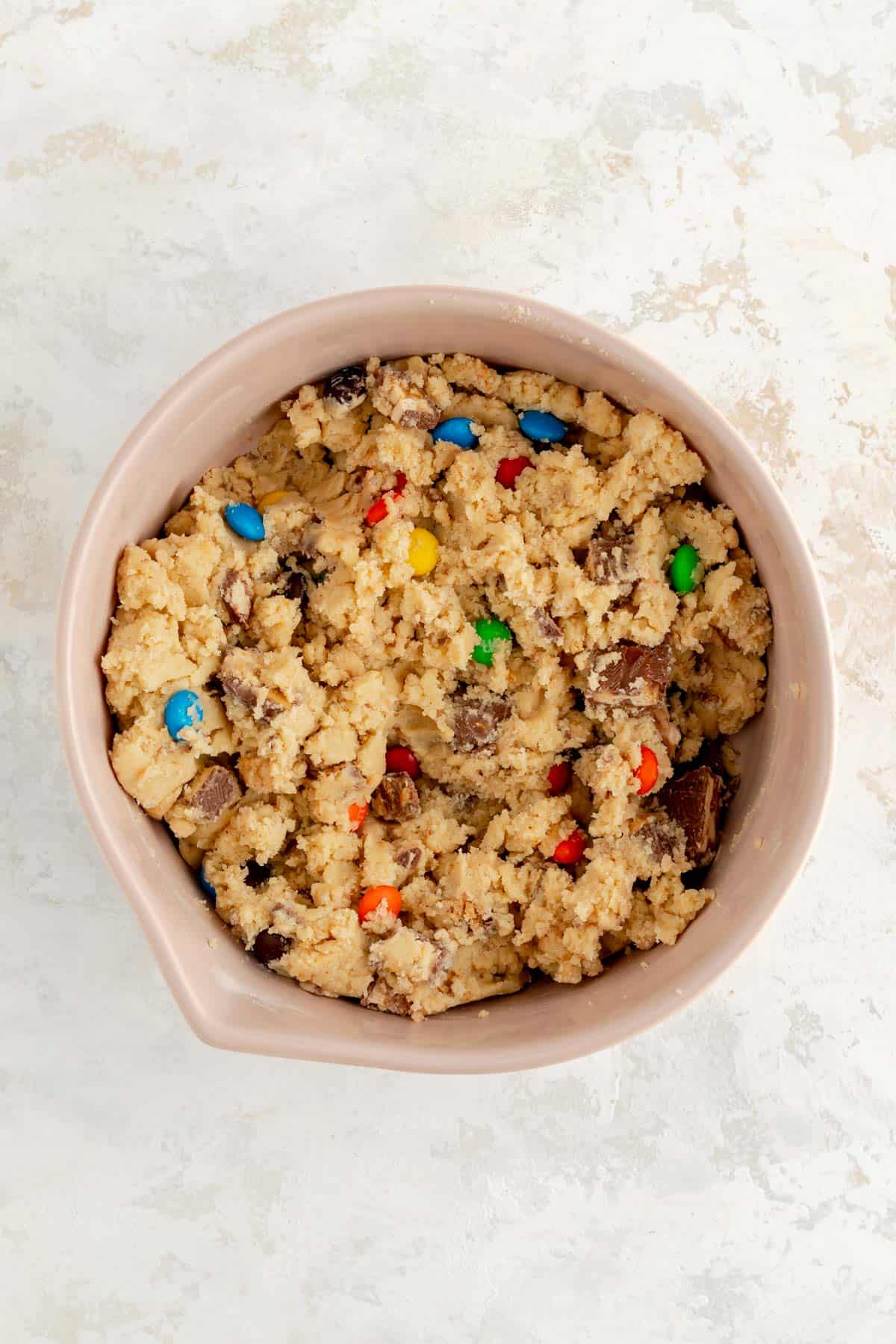 candy bar cookie dough in a tan bowl on white plaster background.